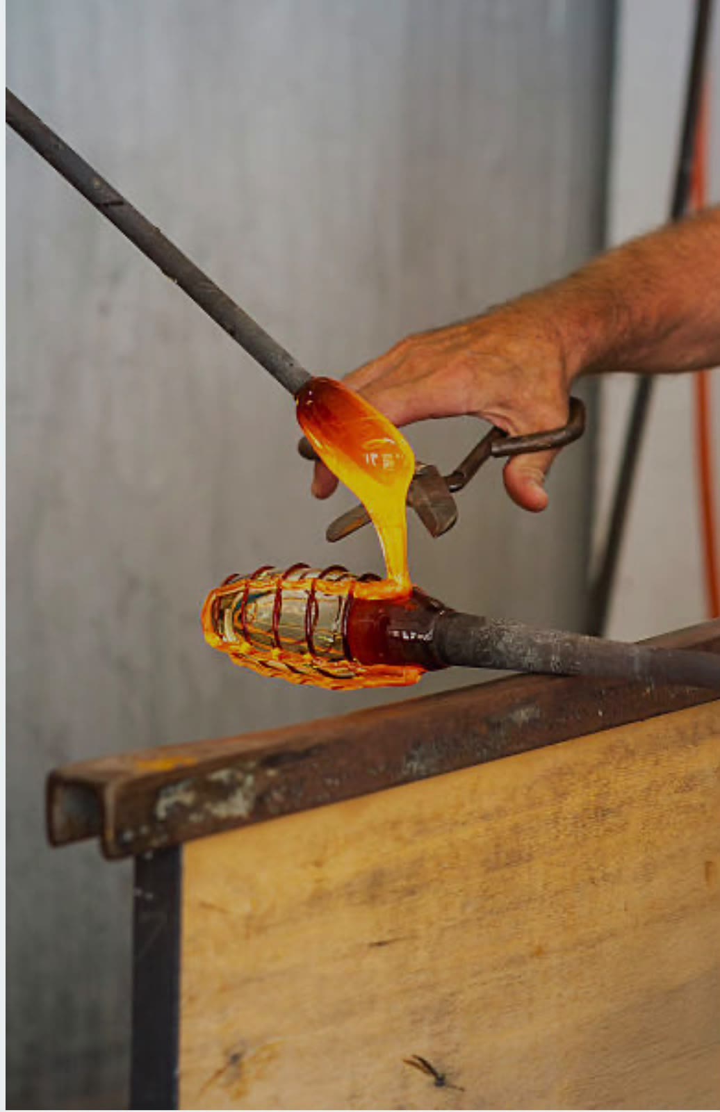 A Murano glass-master drawing a ribbon of molten, glowing glass from the furnace on a long iron rod